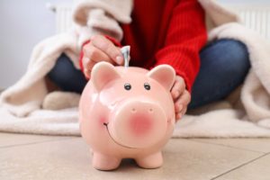 woman in cozy clothes putting cash in piggy bank