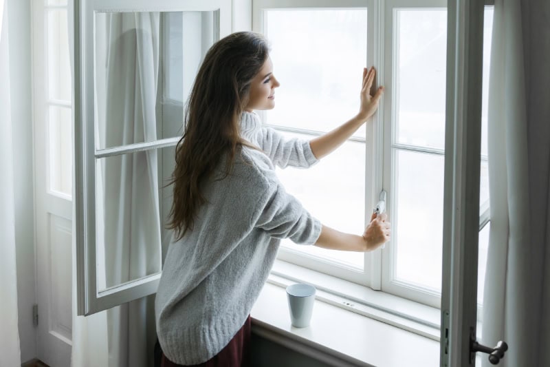 Woman is opening window to look at beautiful snowy landscape outside.
