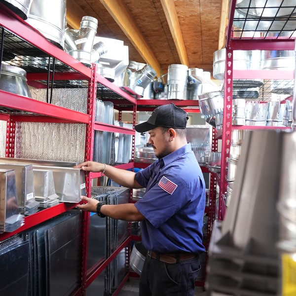 Maki Heating & Air Conditioning technician pulling air duct pieces from a shelf