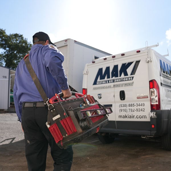 Maki Heating & Air Conditioning technician walking toward the company truck with a tool bag