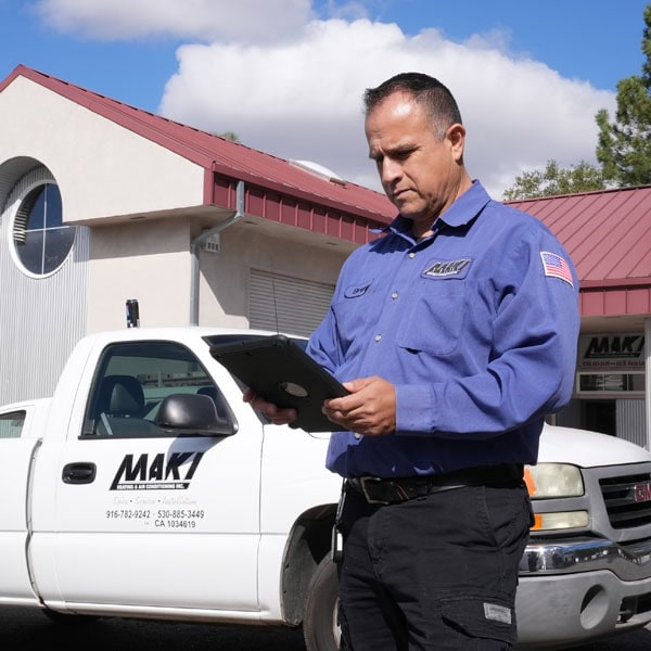 Maki Heating & Air Conditioning technician standing with a clipboard in front of work truck