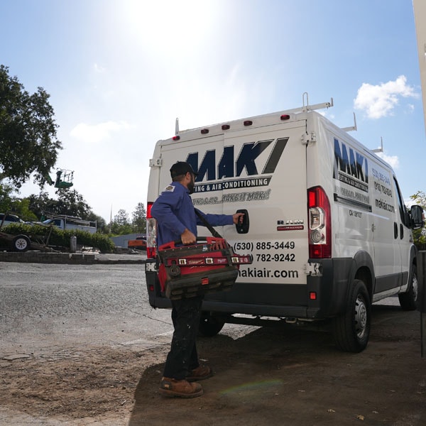Maki Heating & Air Conditioning technician walking with a tool bag to the back of work truck