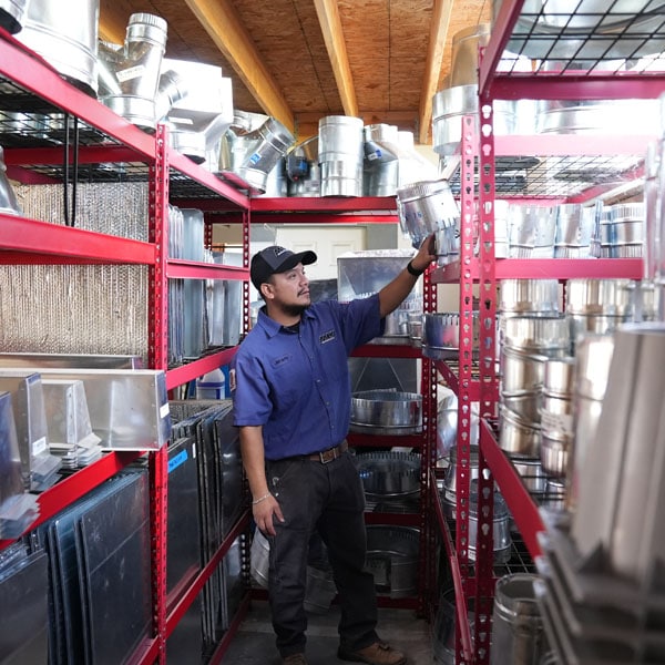 Maki Heating & Air Conditioning technician pulling an air duct piece from a shelf